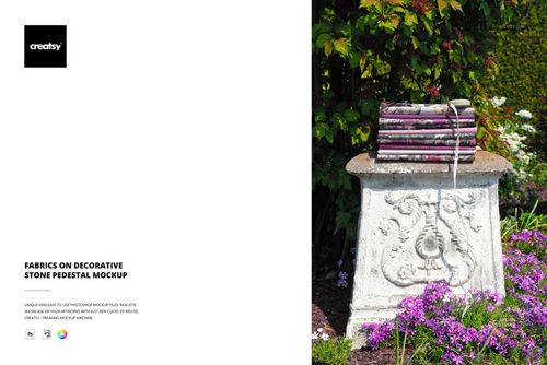 PSD mockup showing folded fabrics on a carved stone pedestal, set among vibrant garden foliage and colorful flowers.