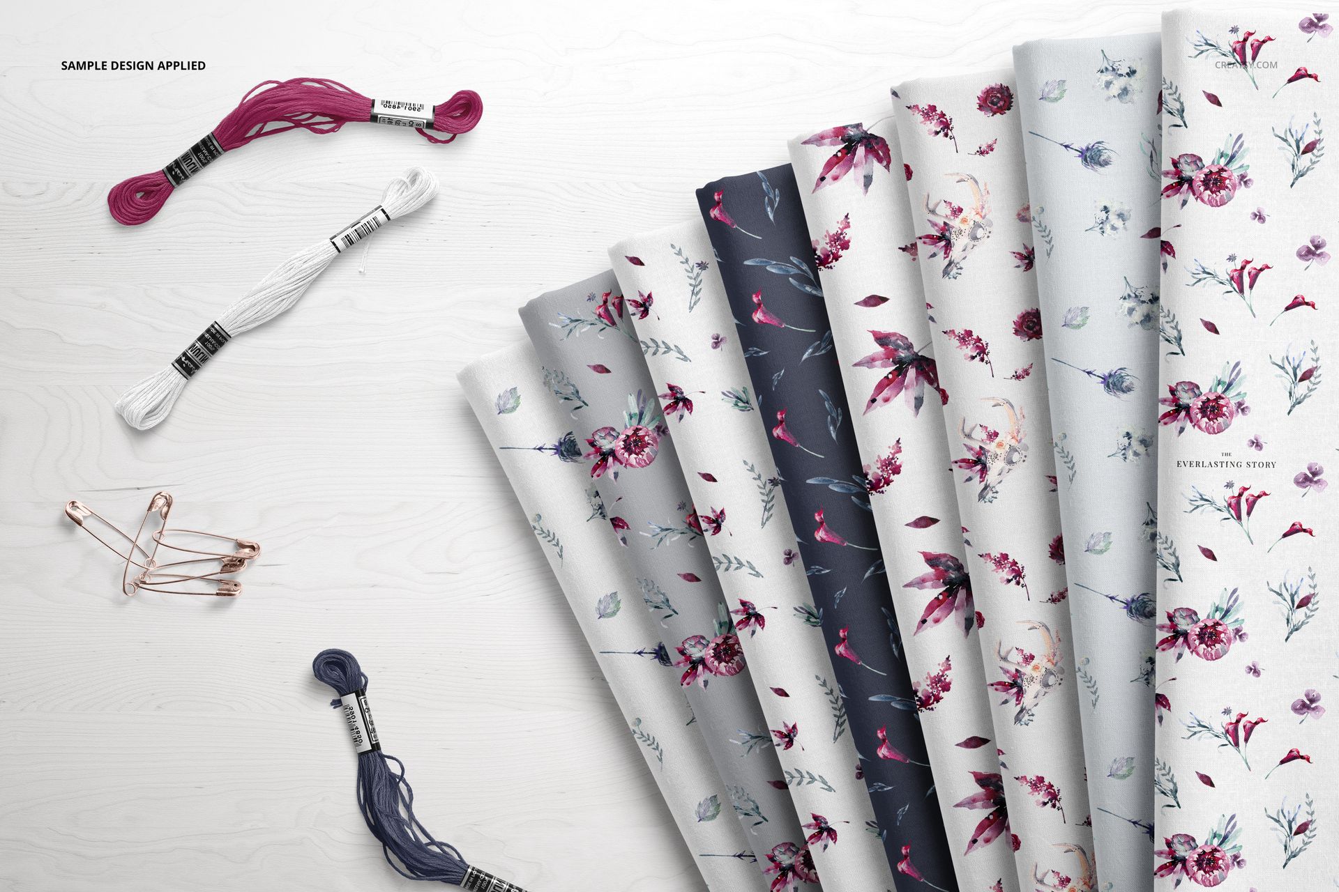 PSD mockup showing several folded textiles with different flower prints, surrounded by embroidery threads and pins.