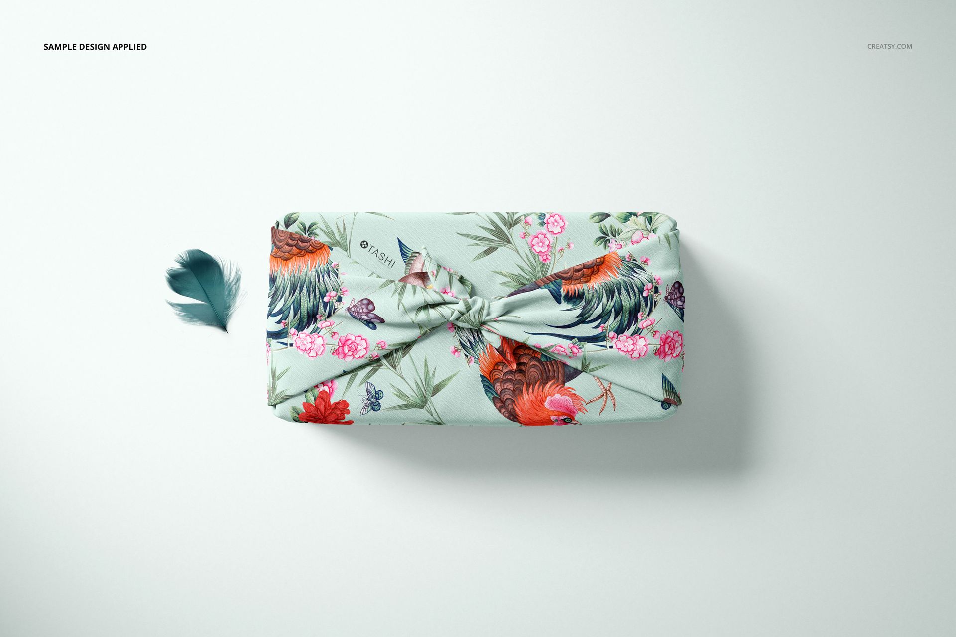 Furoshiki fabric wrap mockup featuring pastel blue textile with colorful roosters and flowers, viewed from above.