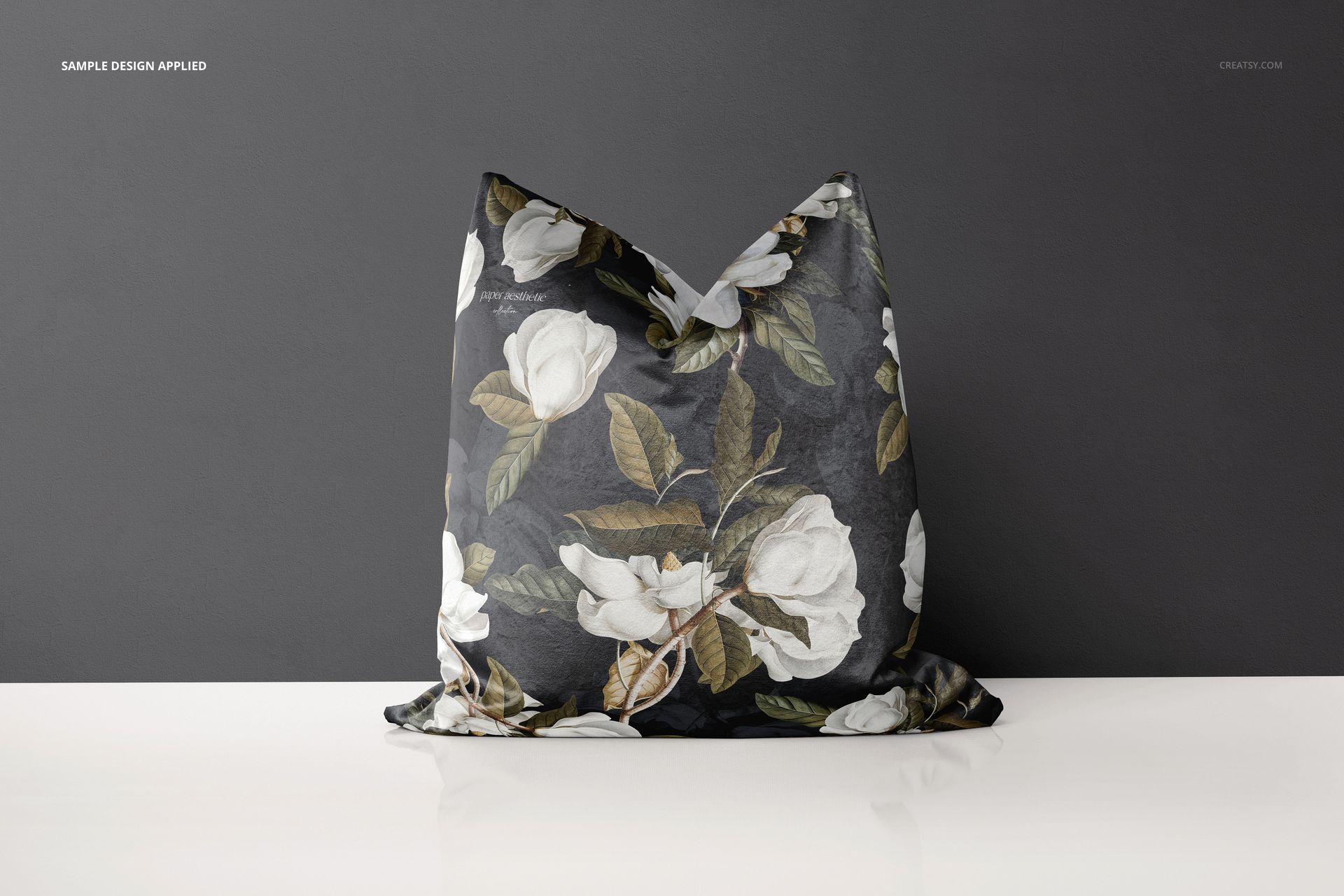 Decorative velvet pillow mockup featuring large white flowers and green leaves, displayed on a white surface.