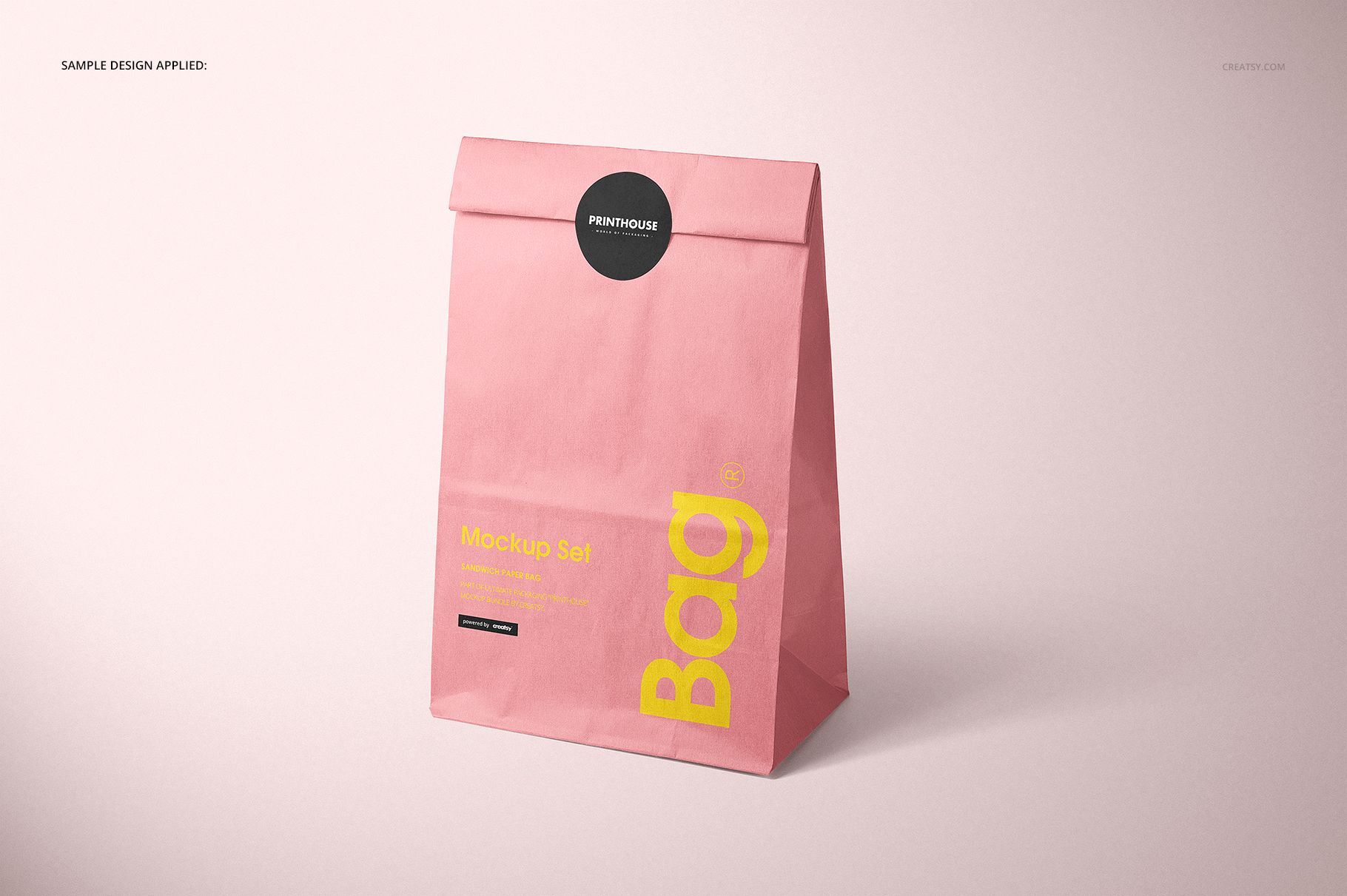 Pink paper lunch bag mockup standing upright, showing a folded top and printed yellow text on a neutral surface.