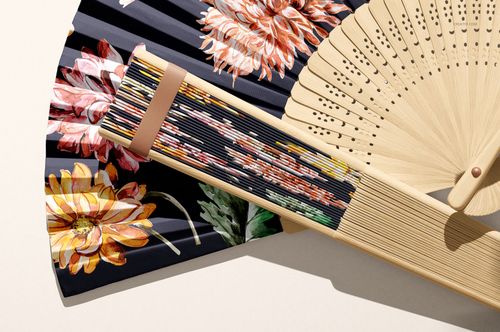 PSD mockup of a fabric hand fan featuring vibrant flower designs, displayed alongside a natural wood fan in close-up.