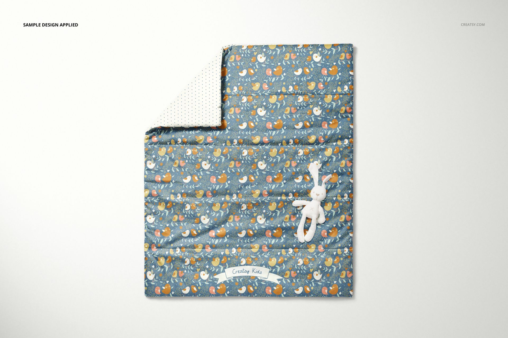 Top view of a baby quilt mockup featuring a colorful animal print and a white stuffed bunny placed on the quilt.