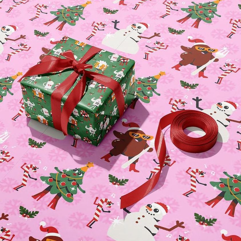 Gift box wrapping paper mockup featuring a green present with red ribbon on pink paper decorated with festive Christmas illustrations.