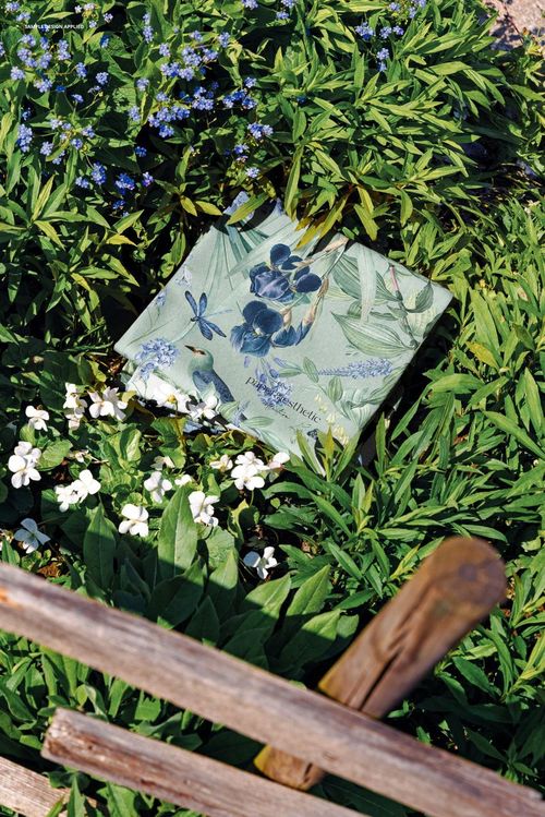 PSD mockup of patterned fabric with blue and green floral motifs lying on a leafy garden ground with white blossoms.