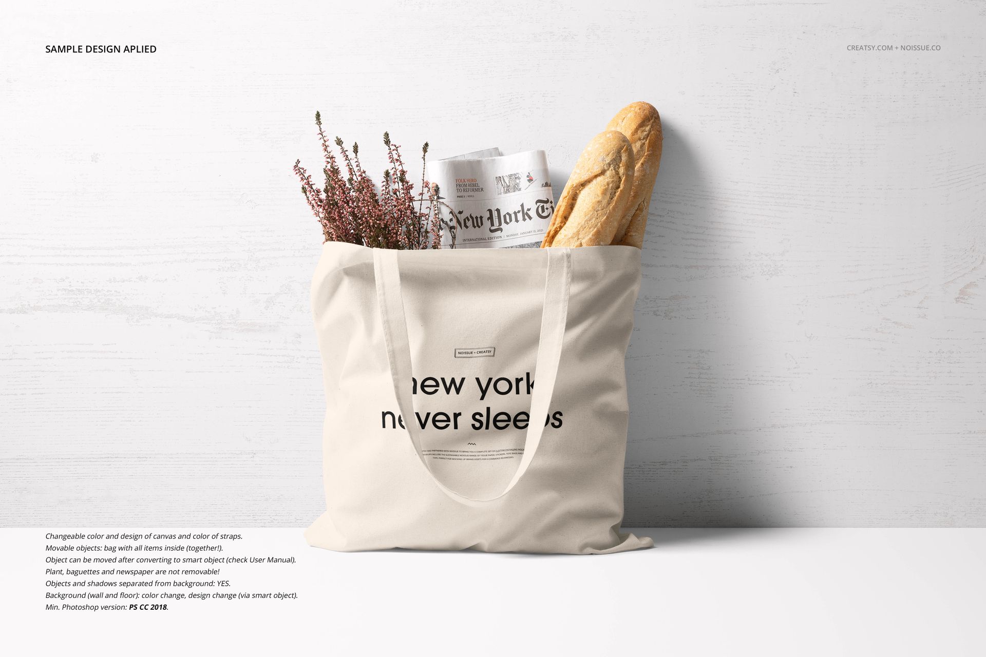 Front view of a beige tote bag mockup on a white surface, filled with a newspaper, lavender stems, and a baguette.