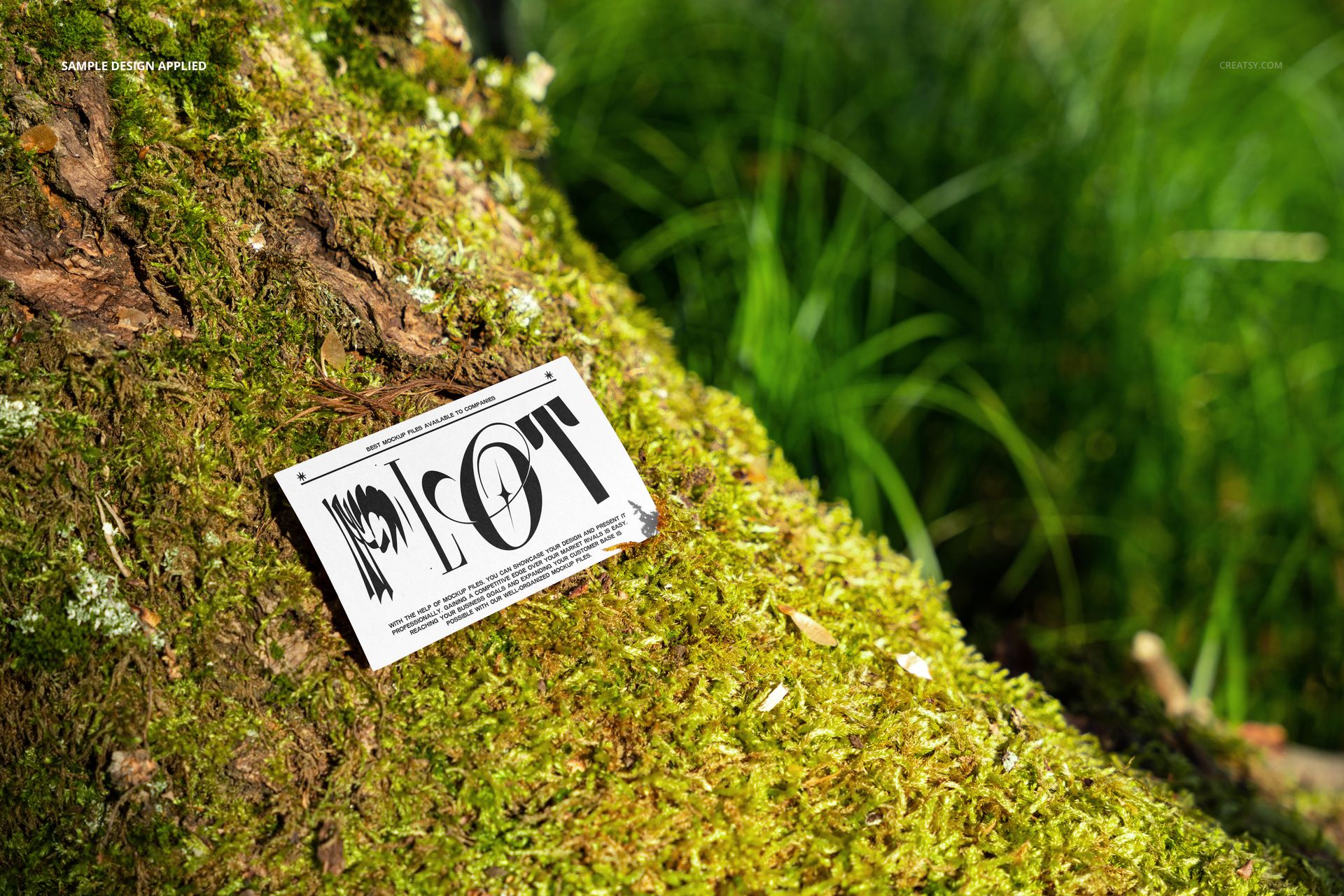 Business card mockup placed on green moss atop a tree trunk, surrounded by grass and forest foliage, side perspective.