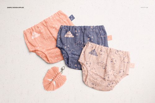 PSD mockup showing baby muslin pants in soft pink, blue, and beige tones with whimsical cloud and moon designs.