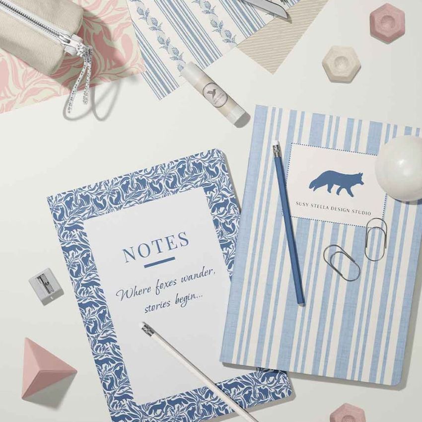 Stationery mockup featuring two classic A4 notebooks on a white surface with pencils, paper clips, and geometric props.