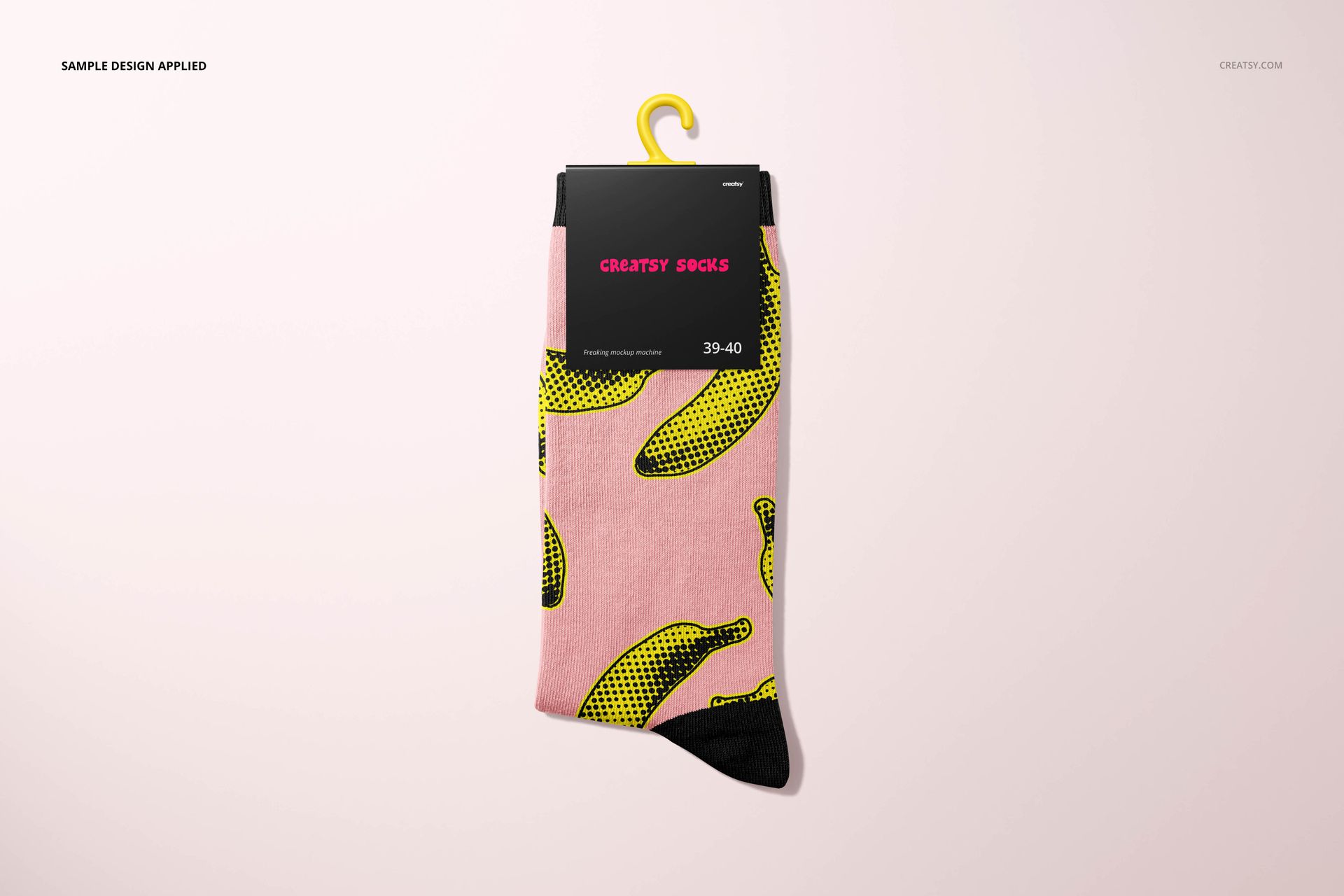 Front-facing sock mockup with a playful yellow banana design on pink fabric, attached to black packaging with a hook.