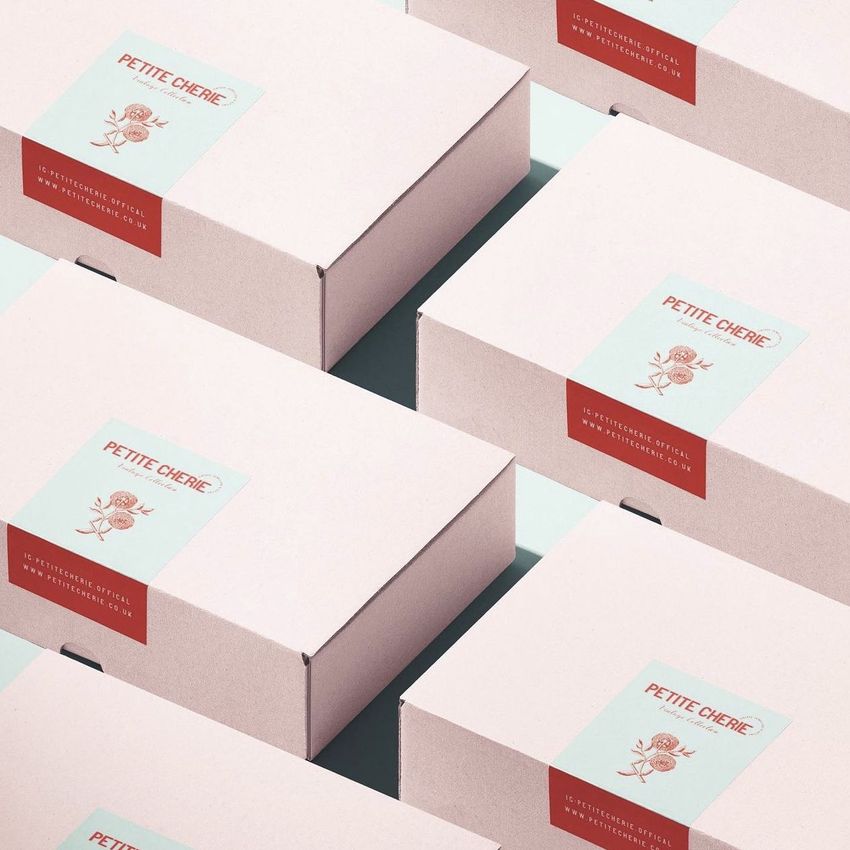 Packaging mockup featuring several light pink boxes with rectangular stickers on the lids, arranged in a diagonal grid on a pale blue surface.