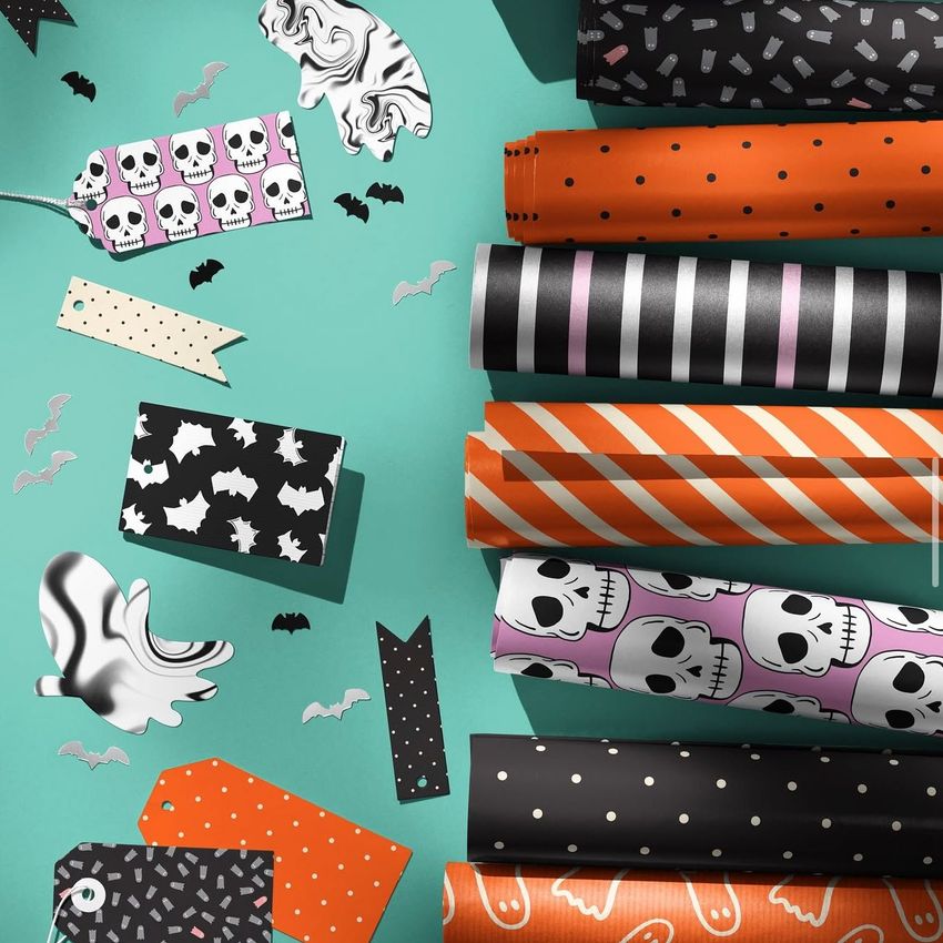 Halloween wrapping paper mockup featuring rolled sheets with skull, bat, and striped patterns, arranged on a teal surface.