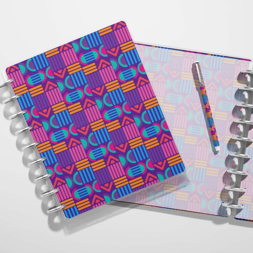 Top view of two spiral planners with bold geometric patterns in purple, orange, teal, and pink on a white surface.
