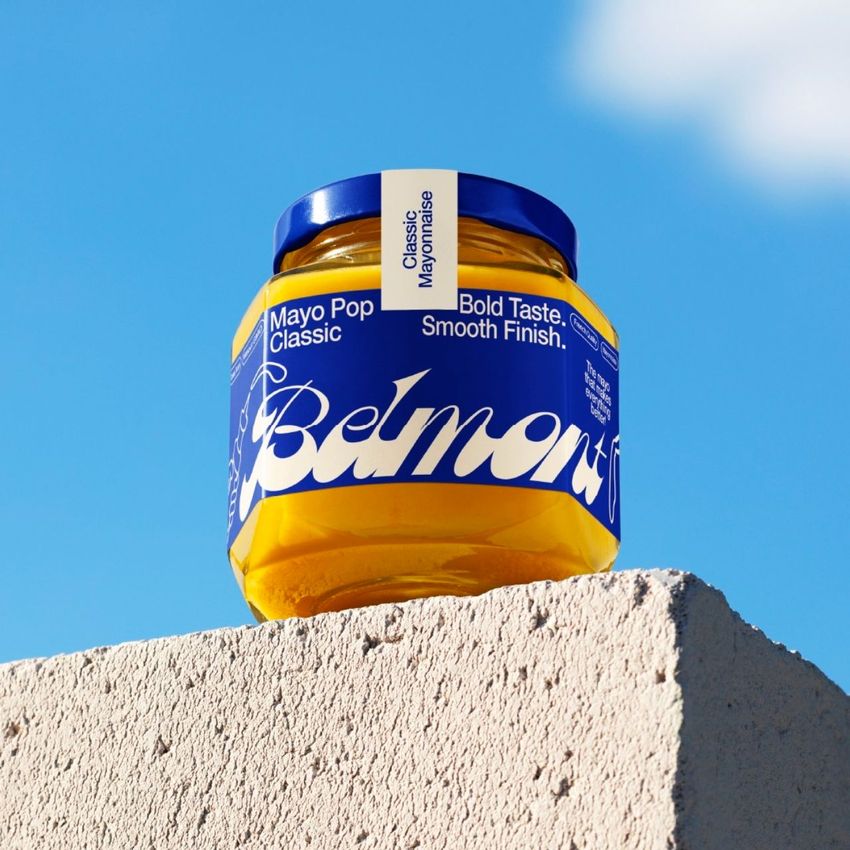 Packaging mockup featuring a mango jam jar with a vibrant label, photographed outdoors on a textured stone surface.