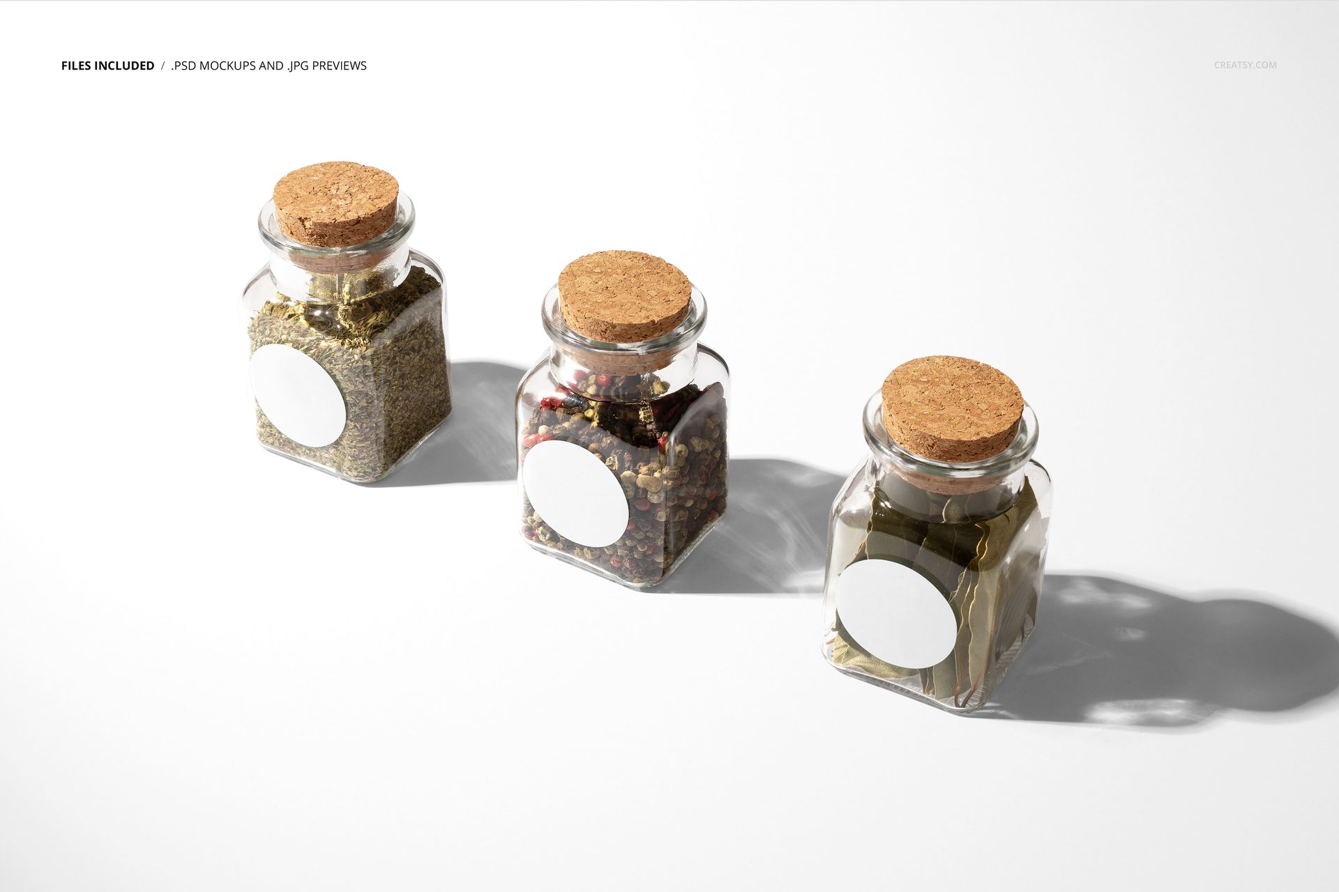 Three square spice jars with cork lids and blank white labels arranged in a row on a white surface in bright light.