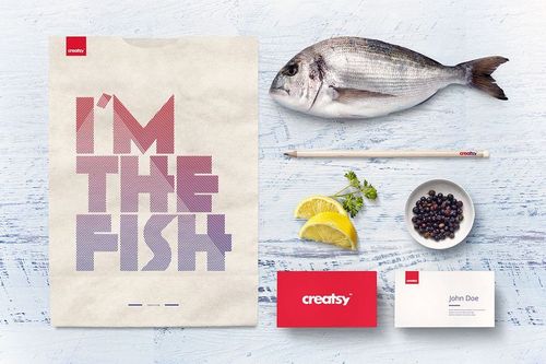 Seafood restaurant mockup set showing a paper bag with geometric text, fresh fish, lemon slices, herbs, and business cards on a light wooden surface.