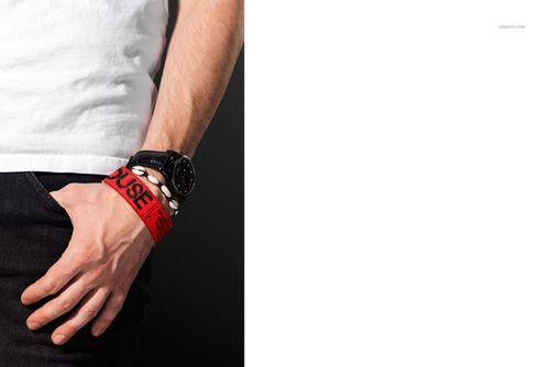 PSD mockup showing a male wrist with a red paper wristband and black watch, photographed from a side angle.