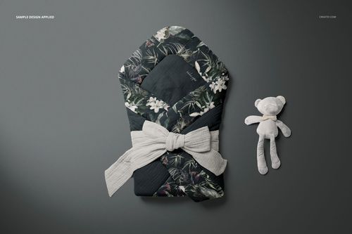 Top view of a muslin baby wrap mockup featuring dark floral design and a soft bow, with a stuffed toy bear nearby.