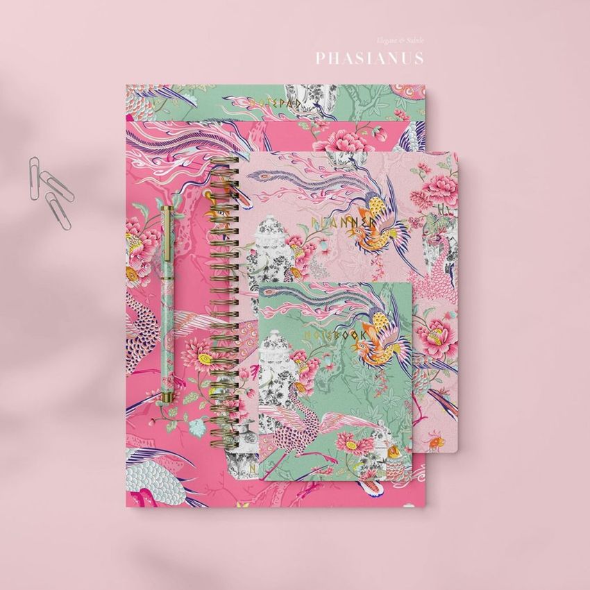Stationery mockup featuring three spiral-bound notebooks with colorful bird and floral patterns on a pink background, shown from above.