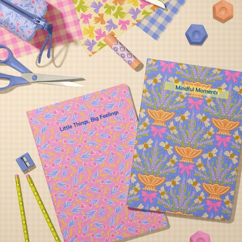 A stationery mockup featuring two A4 notebooks with colorful floral covers on a checkered surface, surrounded by pencils, scissors, and patterned paper.