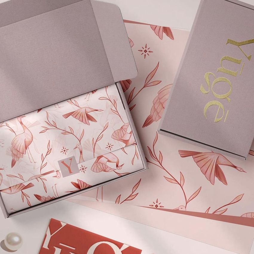 Mailing box mockup with pink and gold accents, featuring floral and bird patterns on tissue paper and packaging inserts.