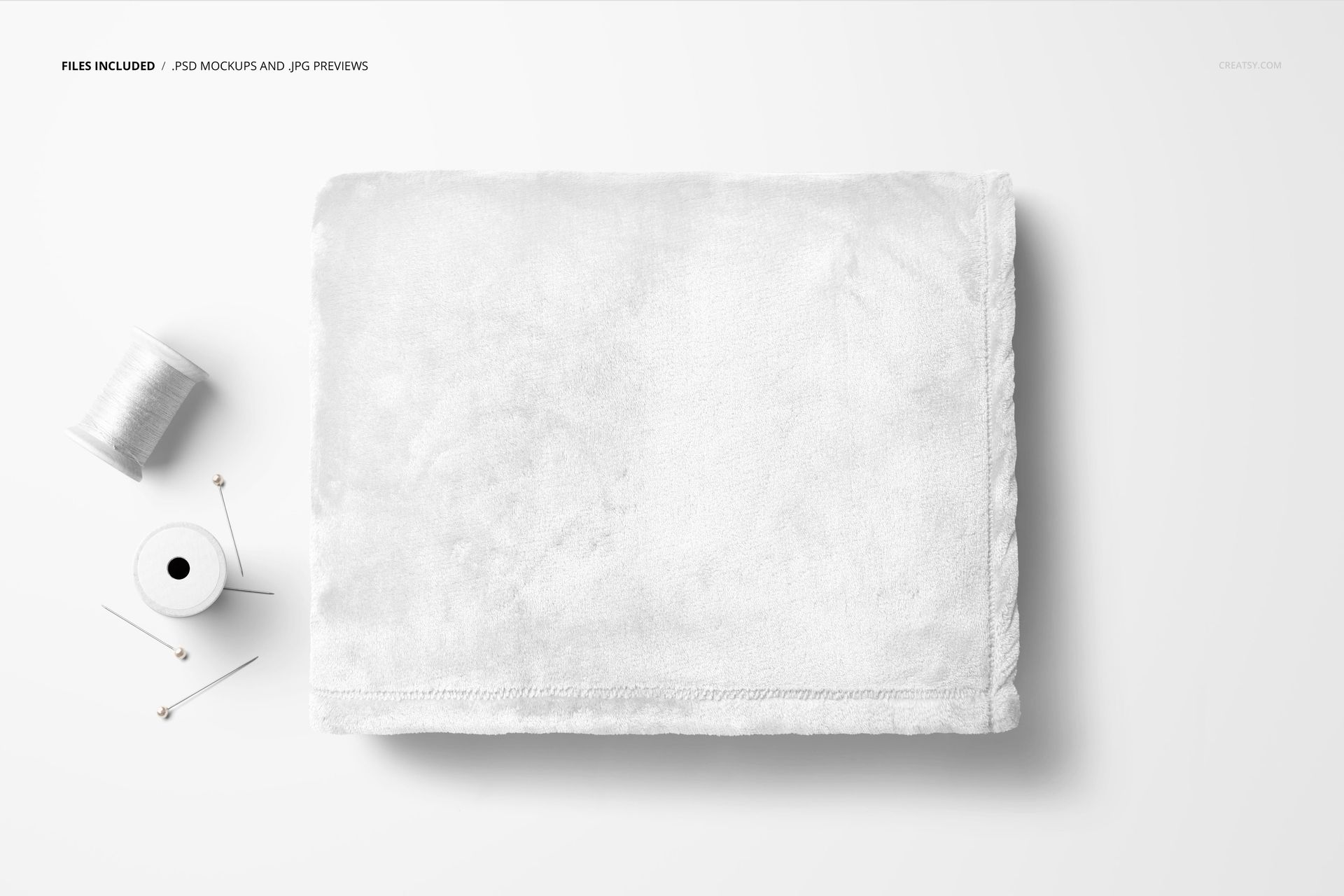 White fleece blanket mockup shown folded neatly with spool of thread and sewing pins on a light background.