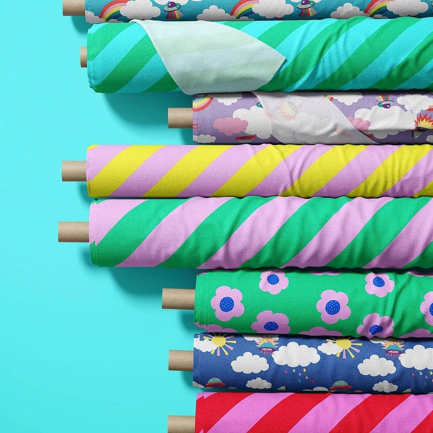 Fabric rolls mockup showing eight colorful rolls with various patterns, including stripes, flowers, and clouds, on a blue background.