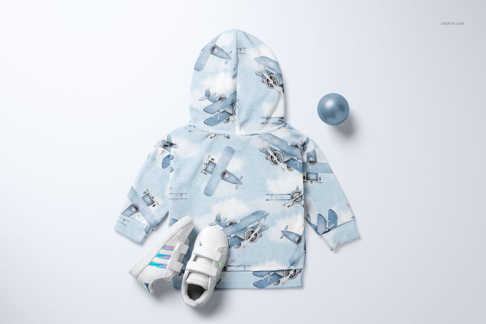 Light blue baby sweatshirt mockup with airplane illustrations, displayed with children’s sneakers and a blue plastic ball.