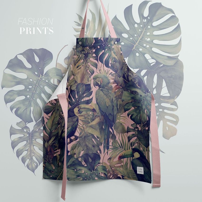 Kids apron mockup featuring a tropical parrot and lush green leaves printed on fabric, displayed against a pale background with leaf graphics.