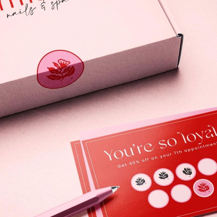 Mailing box mockup on a pink surface next to a loyalty card with circular stamps, a pink pen, and soft shadows.