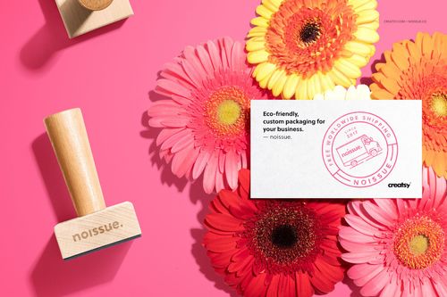 Noissue wooden stamp mockup set shown with vibrant pink, red, and yellow flowers and a branded card on a pink background.