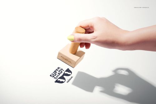 Person using a wooden stamp mockup to apply a blue ink logo on a plain white background, shadow visible.