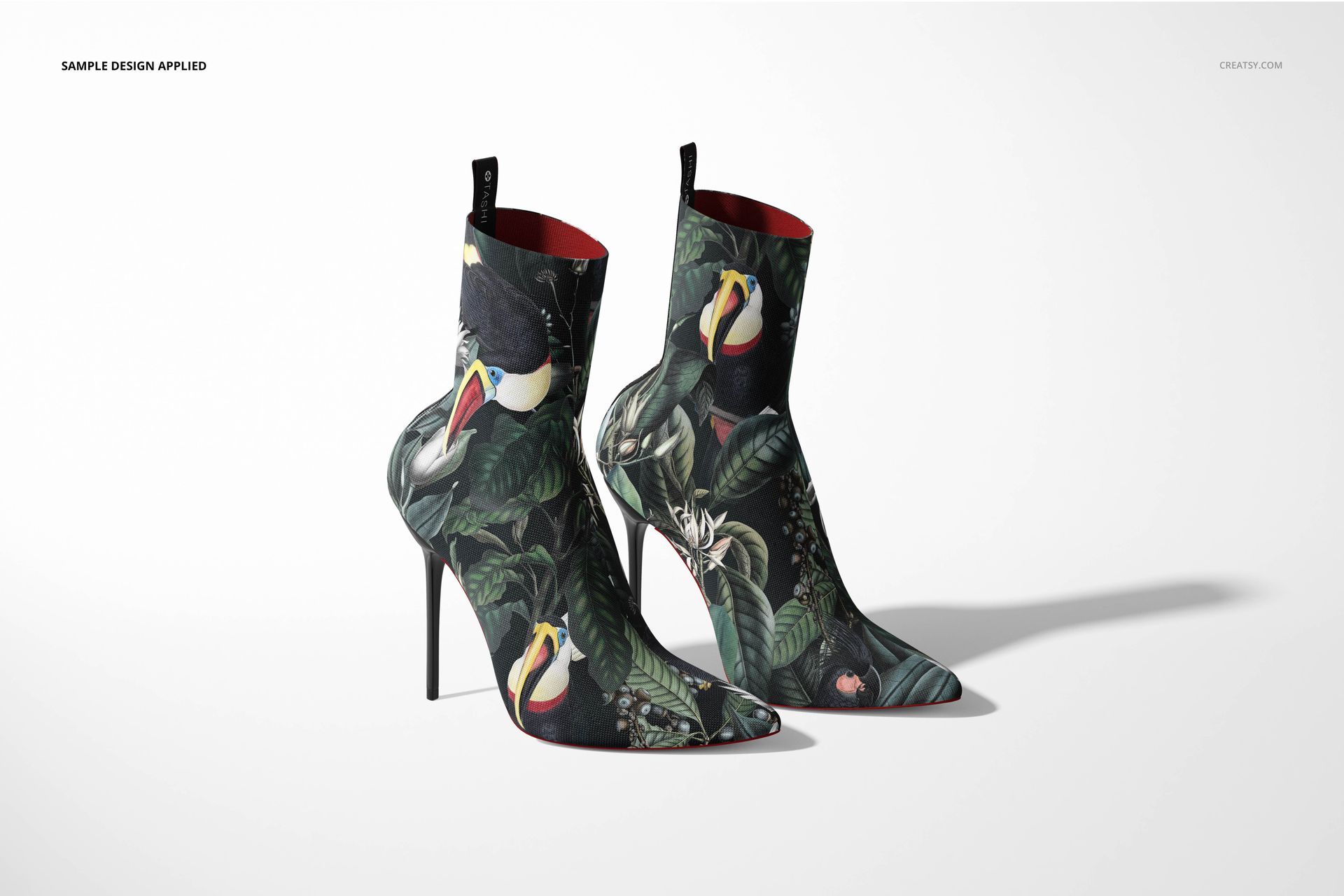 Mockup of ankle boots with high heels, decorated with vibrant jungle motifs and birds, displayed side by side in studio lighting.