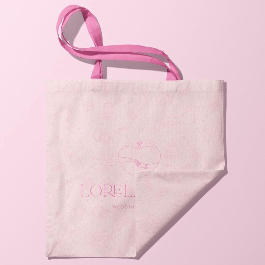 Tote bag mockup featuring a light pink fabric bag with pink handles, subtle line art pattern, and readable text on the front.