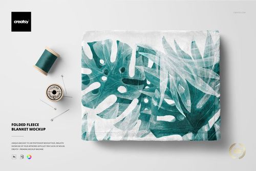 PSD mockup of a folded fleece blanket with a botanical green leaf design, shown from a top view with sewing accessories.