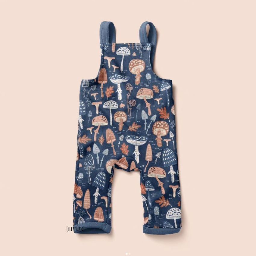 Kids fleece dungarees mockup featuring a whimsical mushroom pattern in earthy tones on a blue background, displayed flat on a light surface.