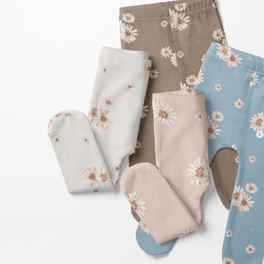 Footed baby leggings mockup featuring four pairs of leggings in beige, blue, white, and pink, each with a daisy floral pattern on a light background.