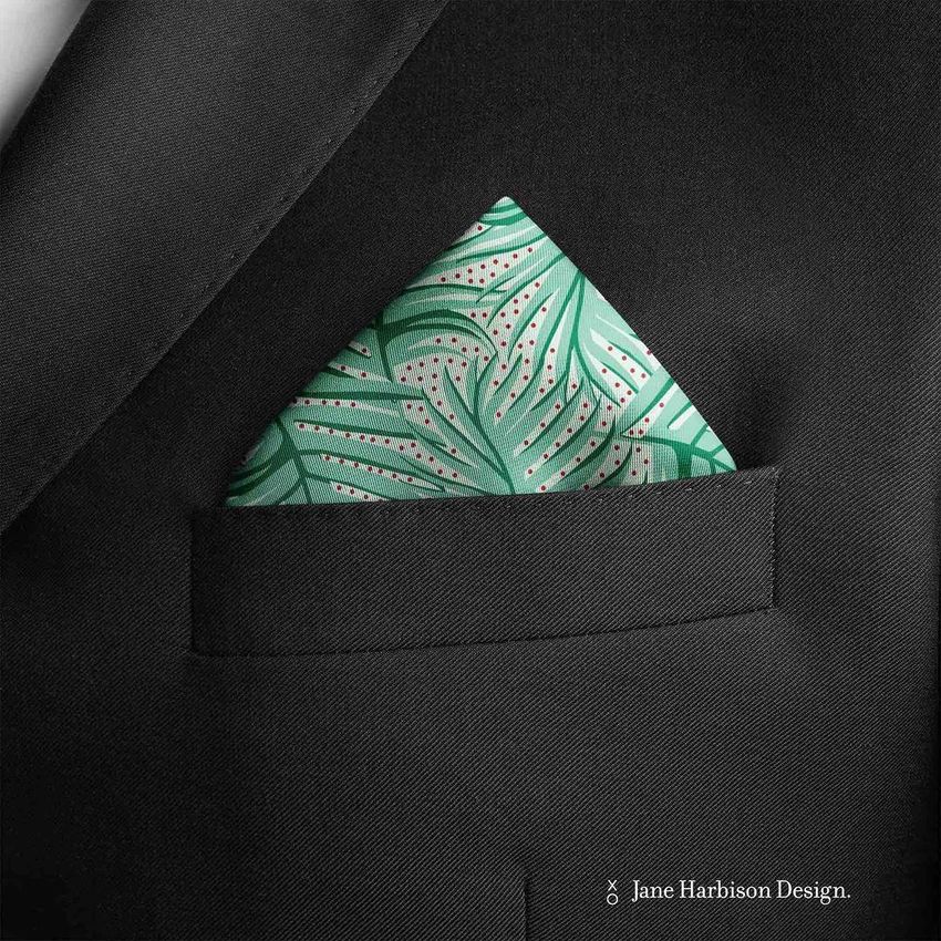 Pocket square mockup showing a green patterned handkerchief with leaf designs in the breast pocket of a black suit jacket.