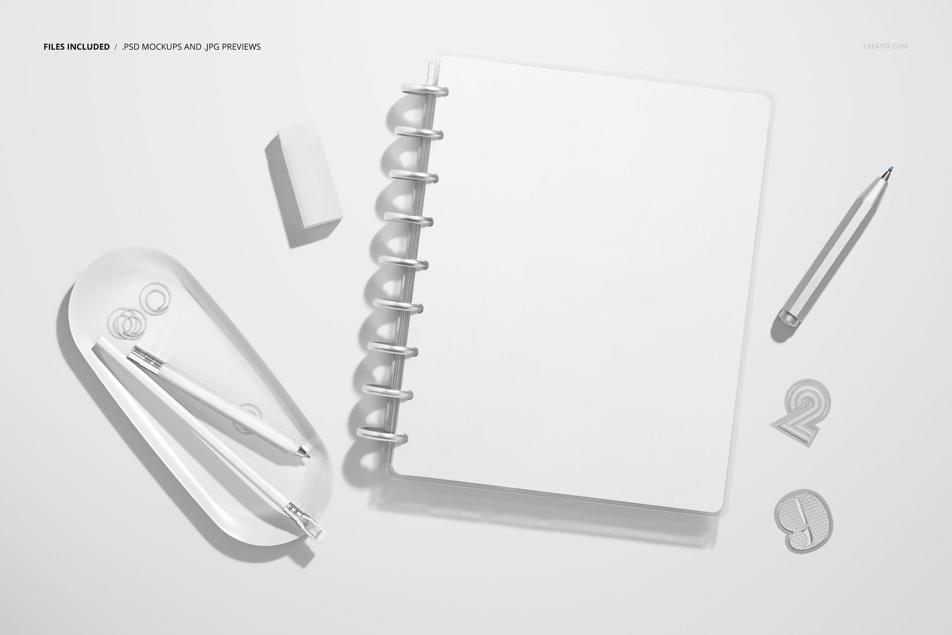 Top view of a spiral planner mockup surrounded by stationery items including pens, eraser, and paper clips on a white surface.