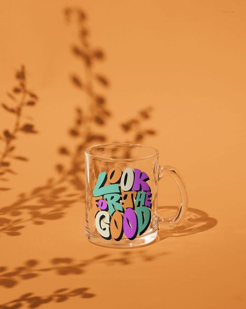 Glass mug mockup displaying bold multicolored text, photographed from the front with leaf-shaped shadows on orange.