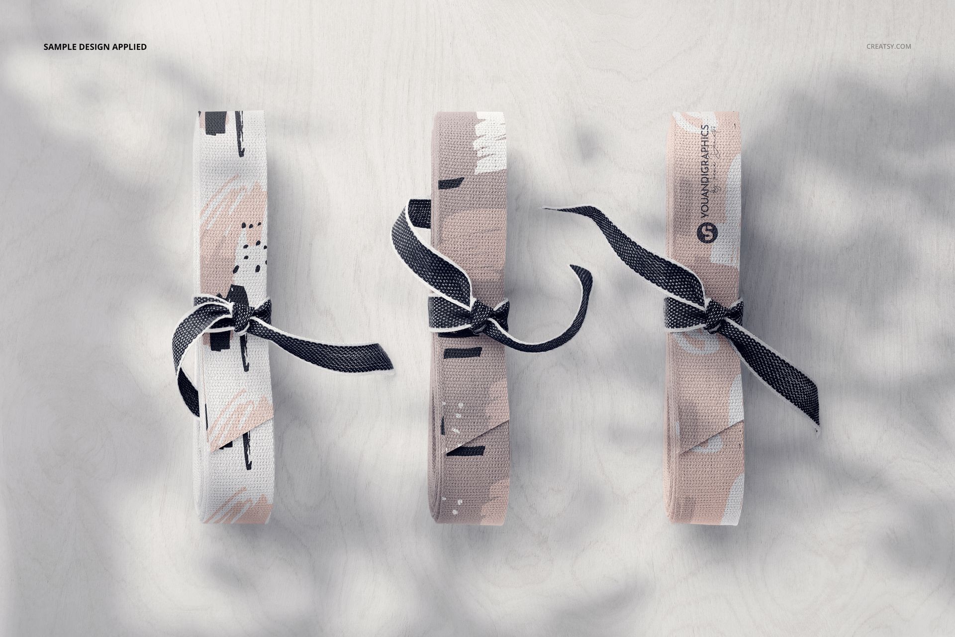 Three cotton ribbon mockups with soft neutral designs and black bows, shown from a top view on a light wooden table.