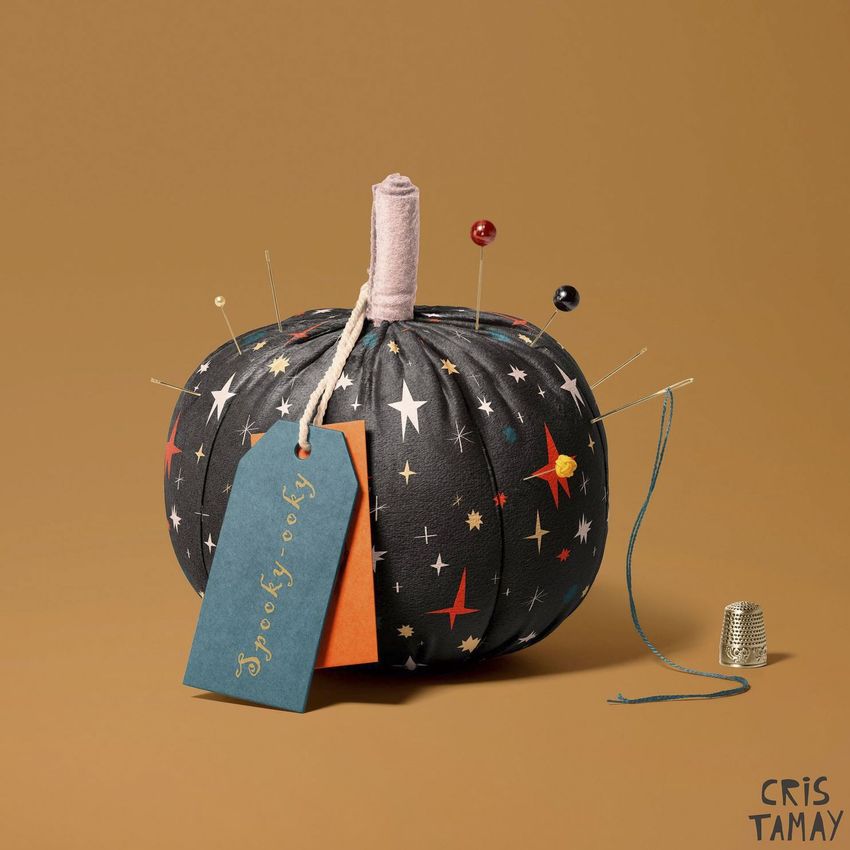 Fabric pumpkin mockup with a dark star-patterned surface, sewing pins, two tags, and a thimble on a brown background.