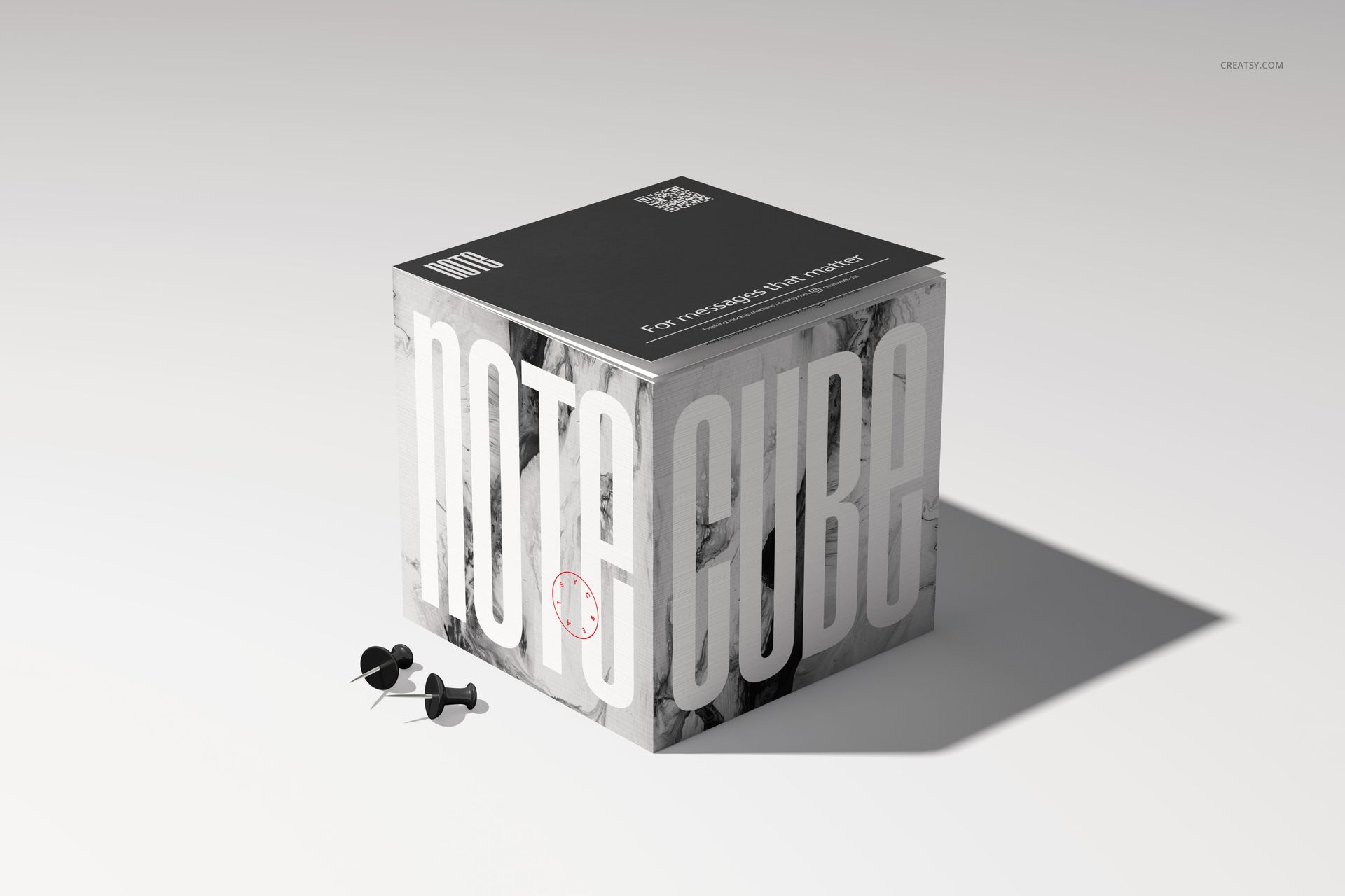 Stationery note cube mockup featuring large vertical lettering, a dark lid, and push pins beside the cube.