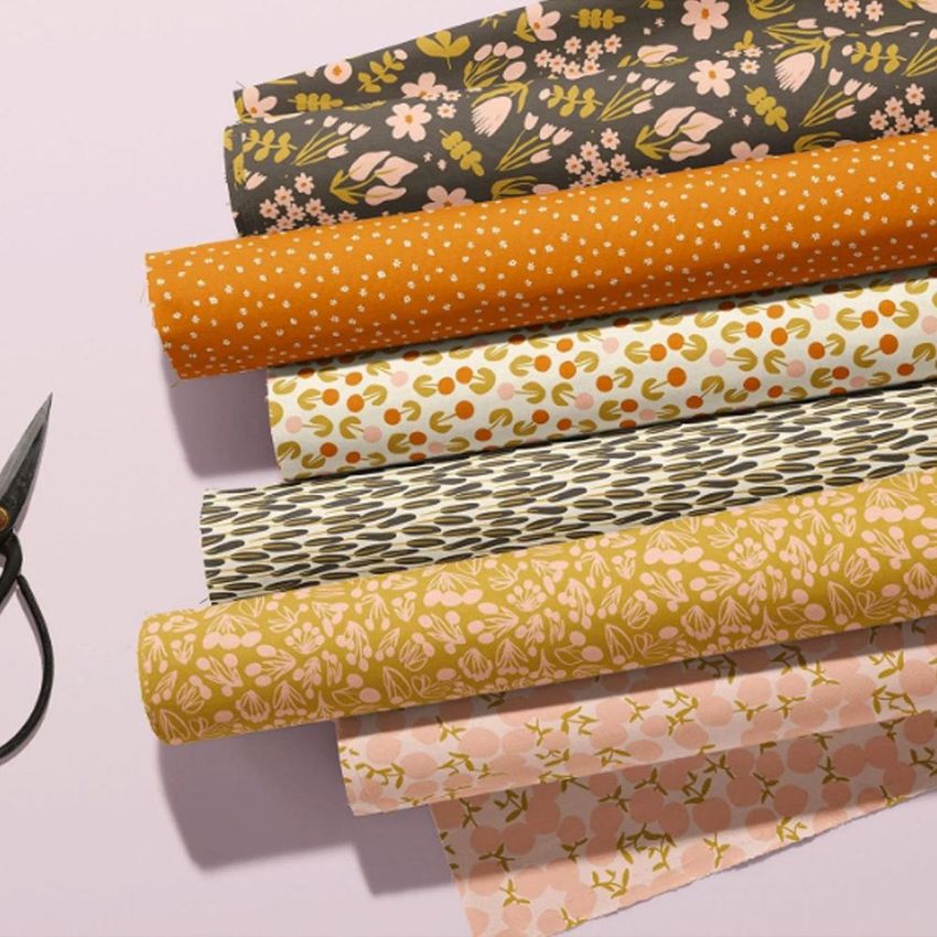 Fabric rolls mockup featuring six patterned fabrics in floral and geometric designs, arranged diagonally on a light surface.