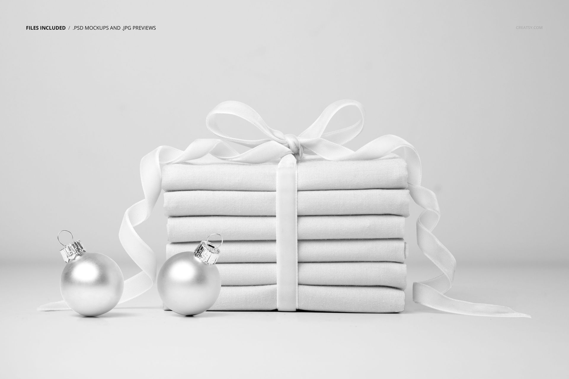 Stacked fabric mockup arranged as a gift, with a velvet ribbon and two metallic baubles on a plain background.