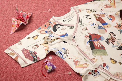 Organic cotton baby kimono bodysuit mockup with vibrant cultural motifs, displayed flat on a red patterned background.
