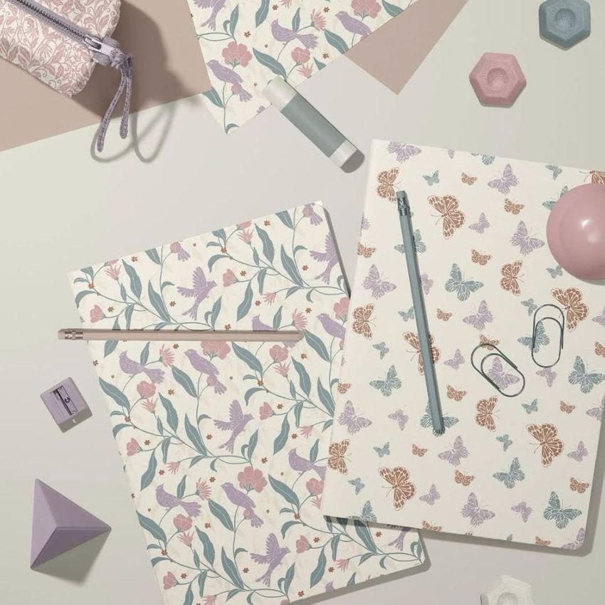Stationery mockup featuring two A4 notebooks with pastel floral and butterfly patterns, surrounded by geometric props and office supplies.