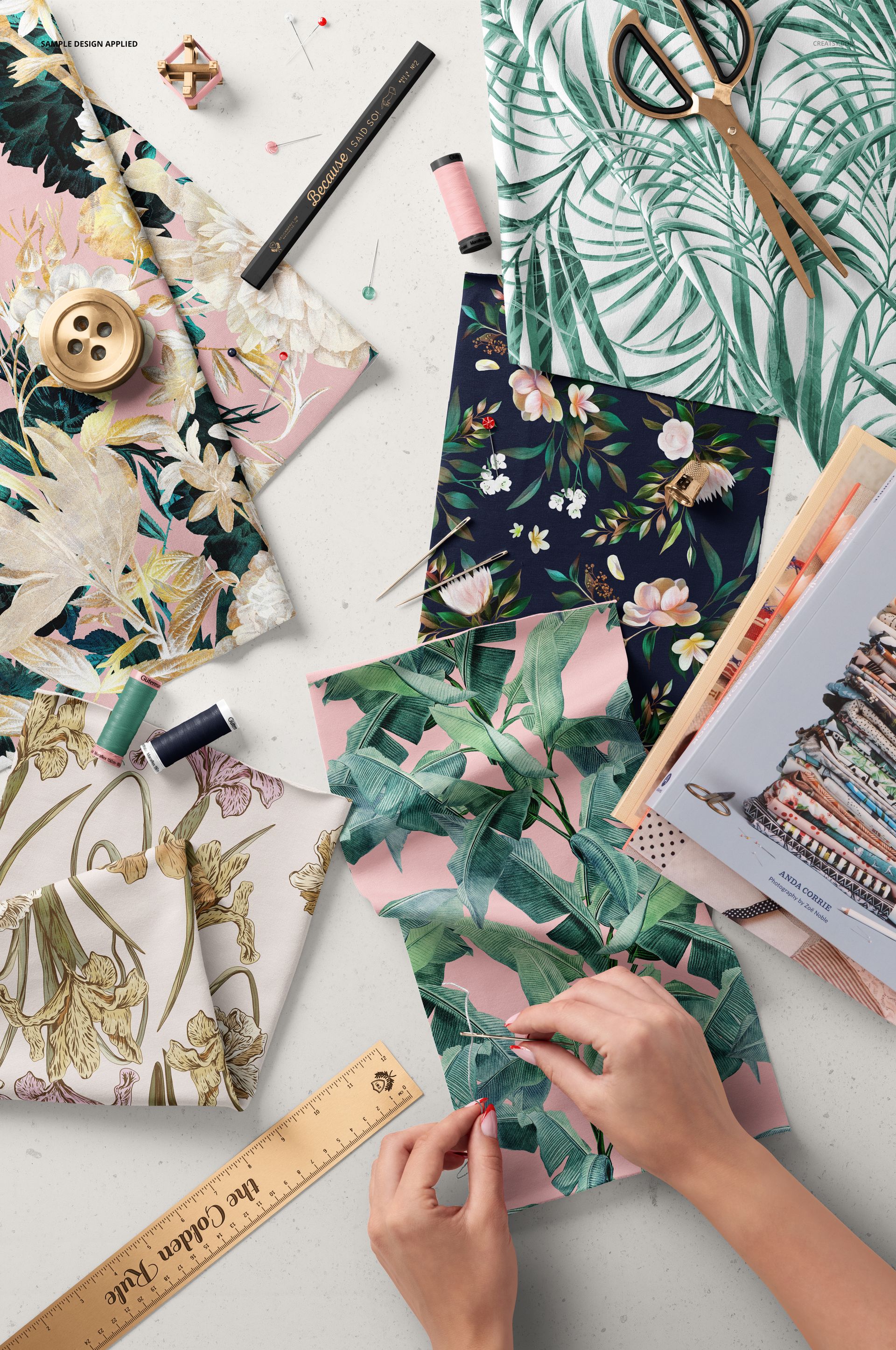 Assorted colorful fabric swatches, sewing accessories, and hands working on a PSD mockup scene viewed from above.