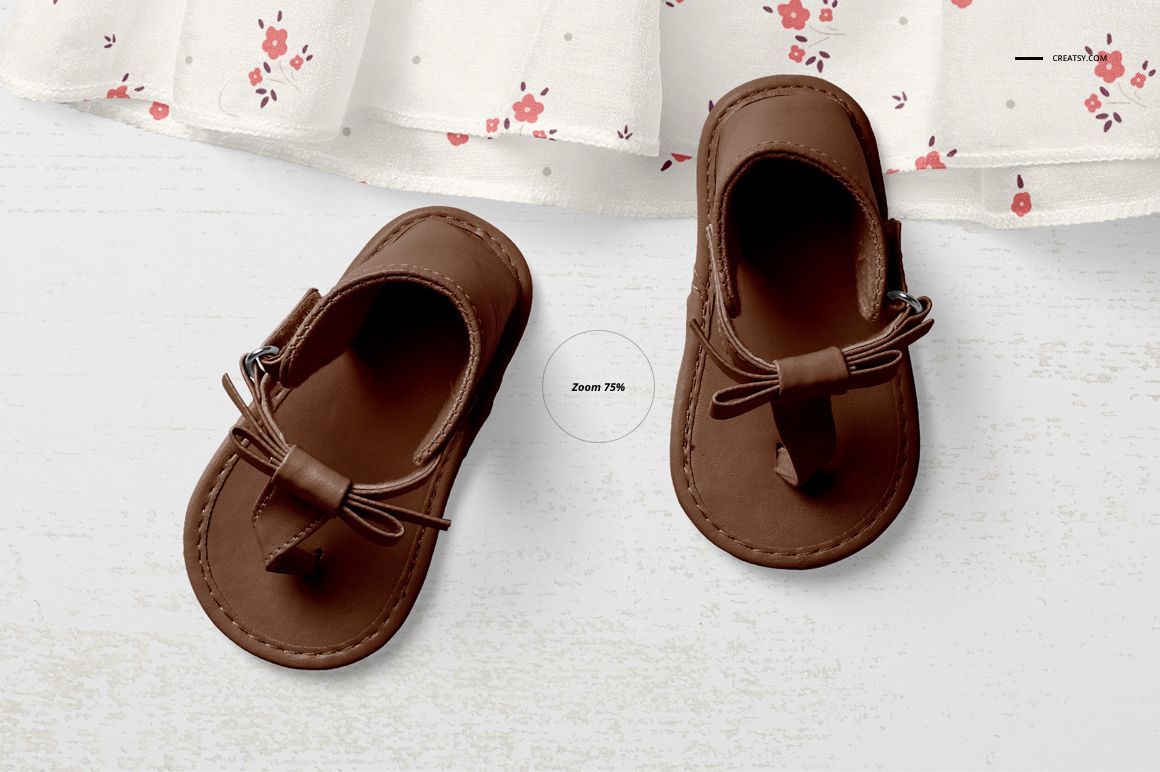 Top view of brown baby moccasins placed on a white wooden surface near a white fabric with small red floral pattern.