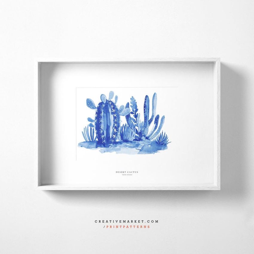 Wooden picture frame mockup featuring a blue watercolor cactus print centered on a white wall with subtle shadow.